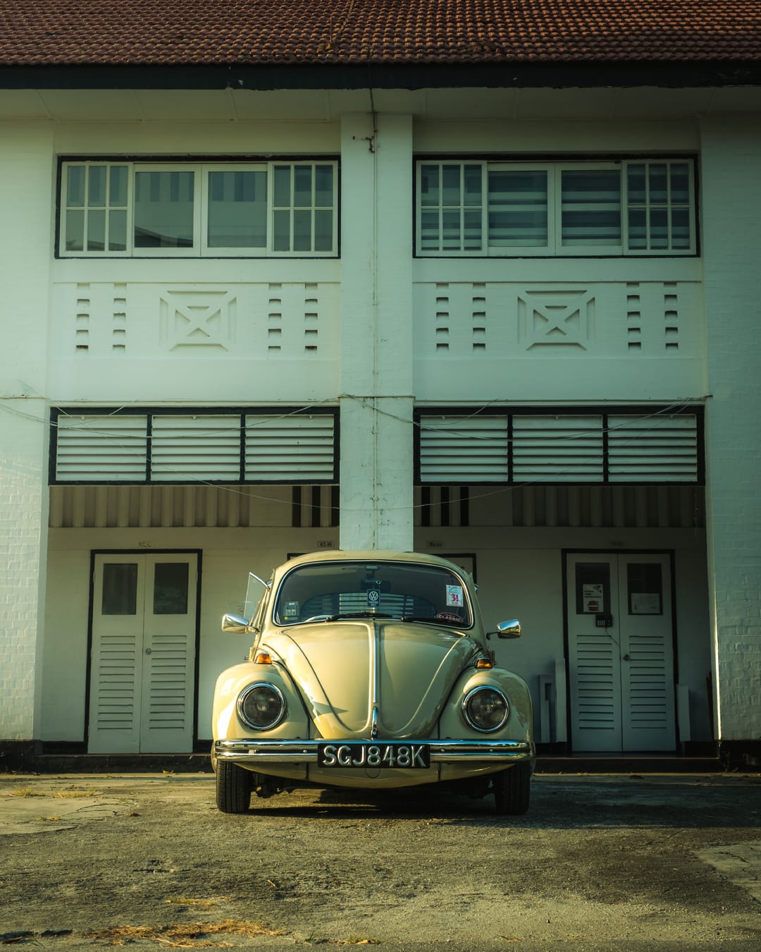 A cream 1968 Volkswagen Beetle parked head on outside a white colonial shophouse