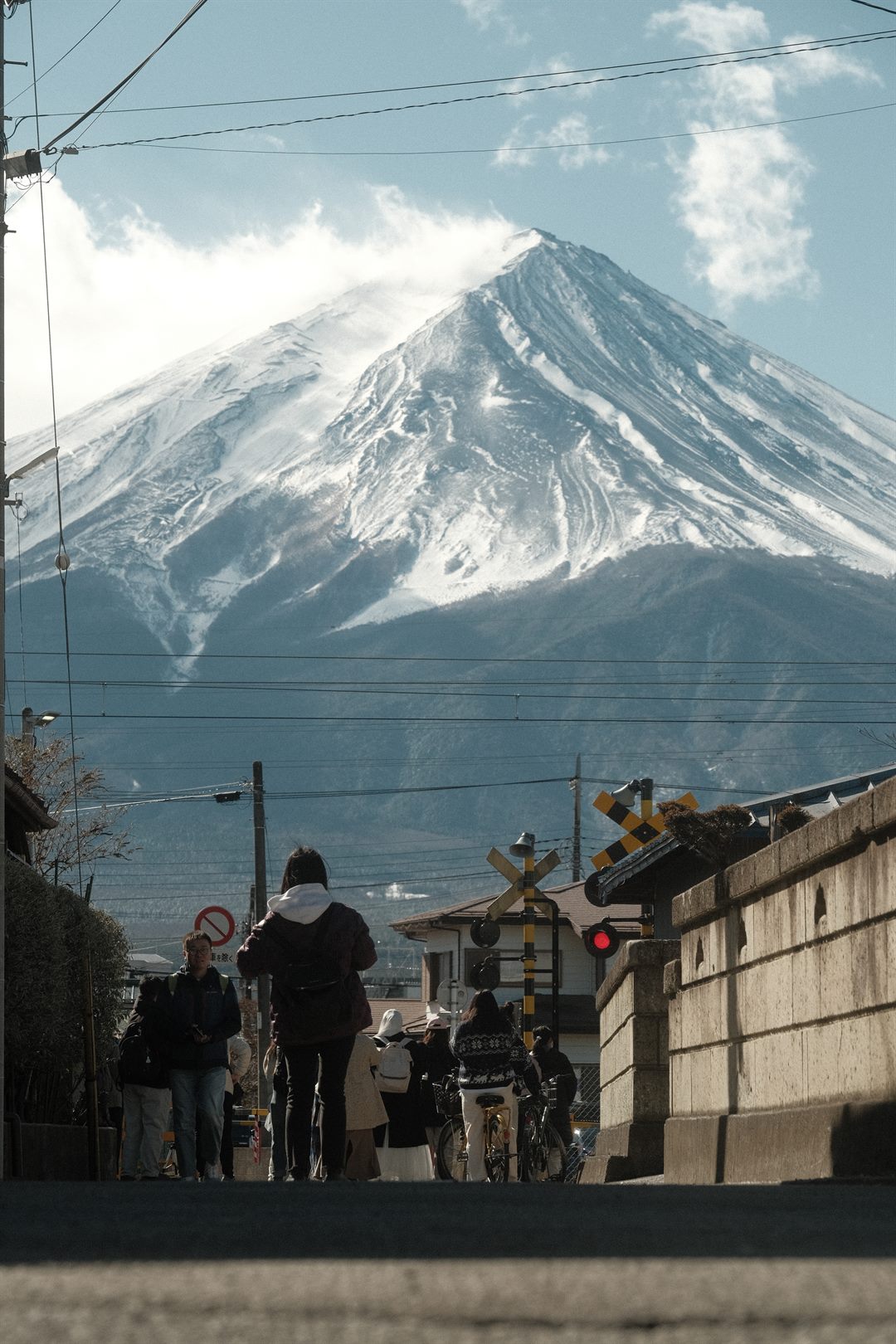 People waiting at a railway crossing on a hill, Mount Fuji rising directly ahead
