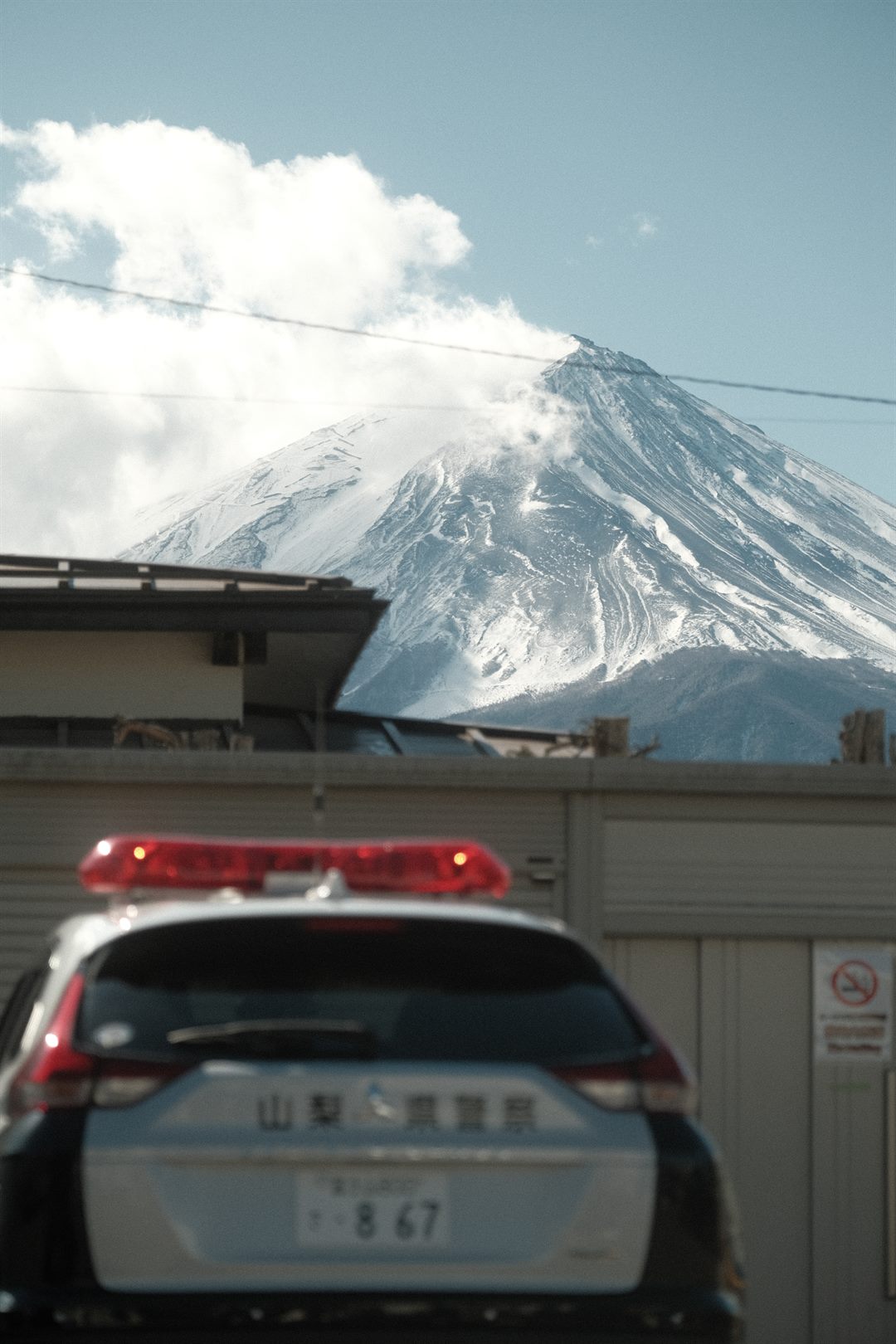 A police car parked below Mount Fuji, the mountain sharp behind a blurred foreground