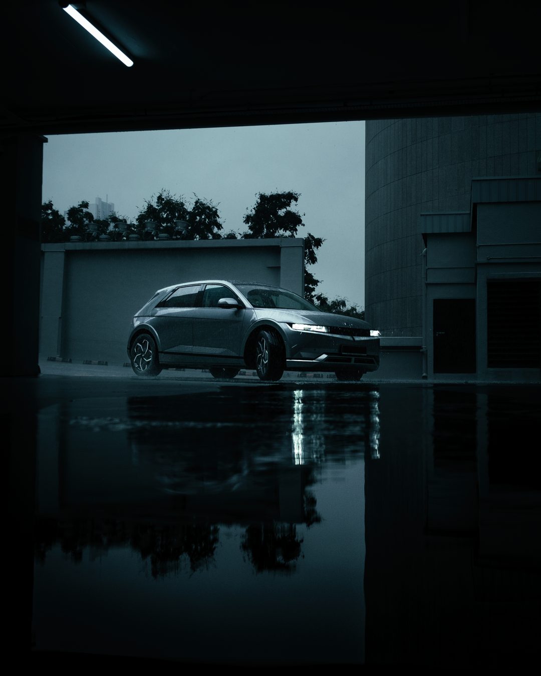 A silver Hyundai Ioniq 5 on a wet deck, framed by a dark garage opening with its reflection in the water below