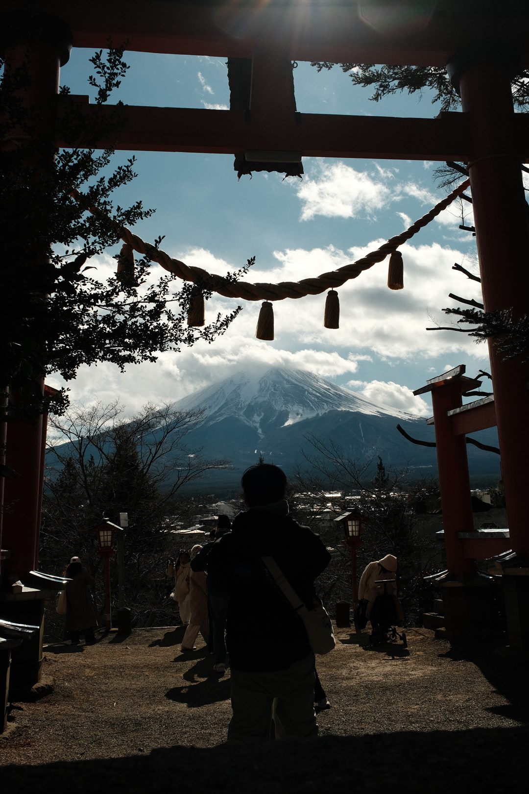 A shrine gate silhouetted against the sky, Mount Fuji beyond and a visitor looking out