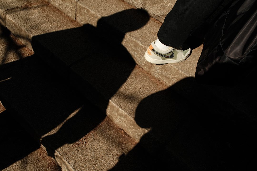 Long shadows of two people fall across stone steps beside a single sneakered foot