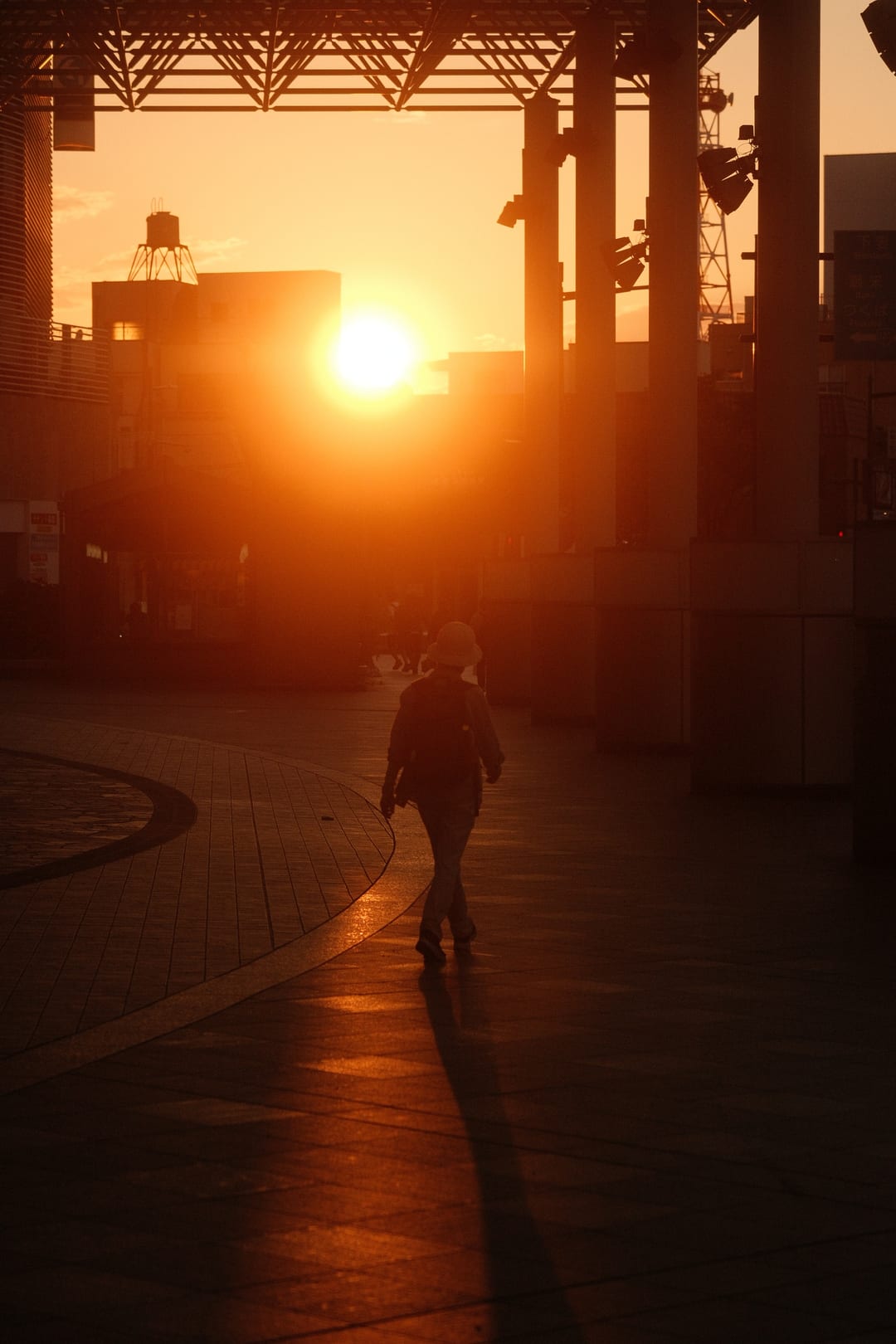 A person walking straight into the setting sun on a station deck