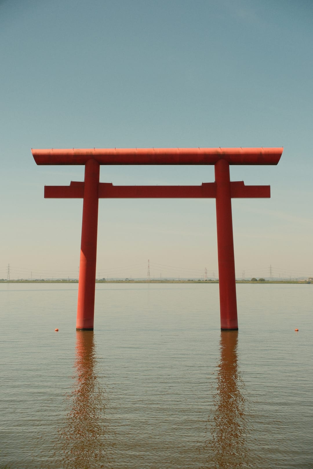 A red torii gate standing in calm shallow water under a pale sky