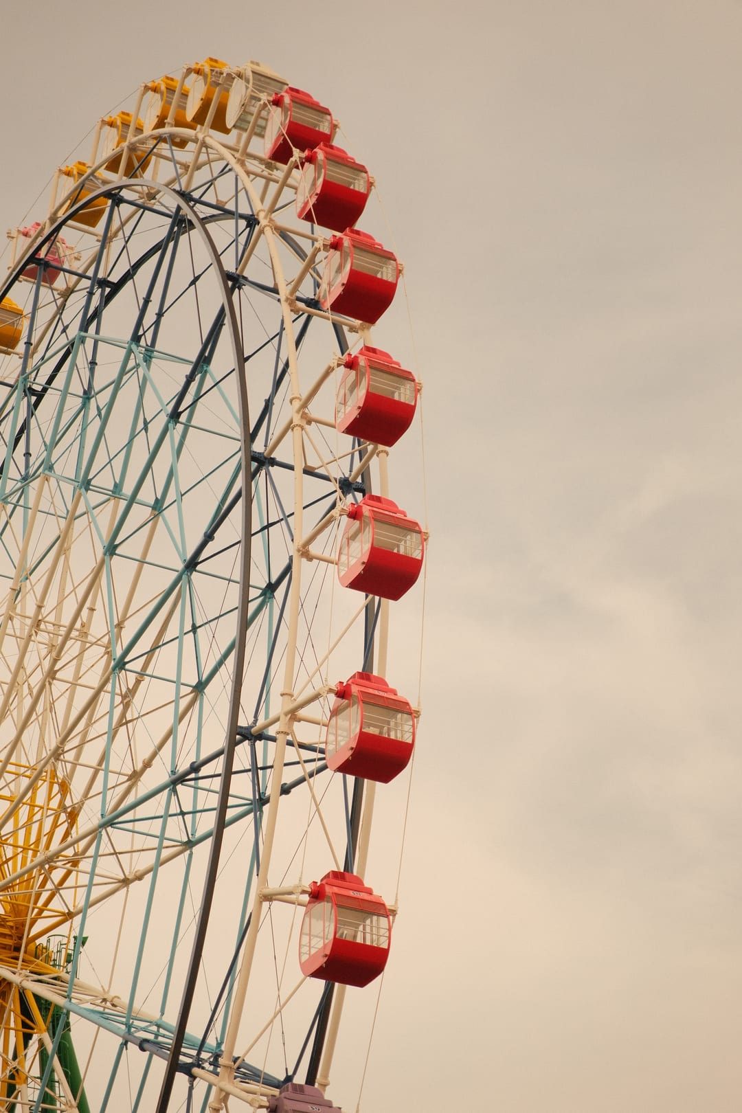 Red and cream gondolas curving away on a ferris wheel against flat sky