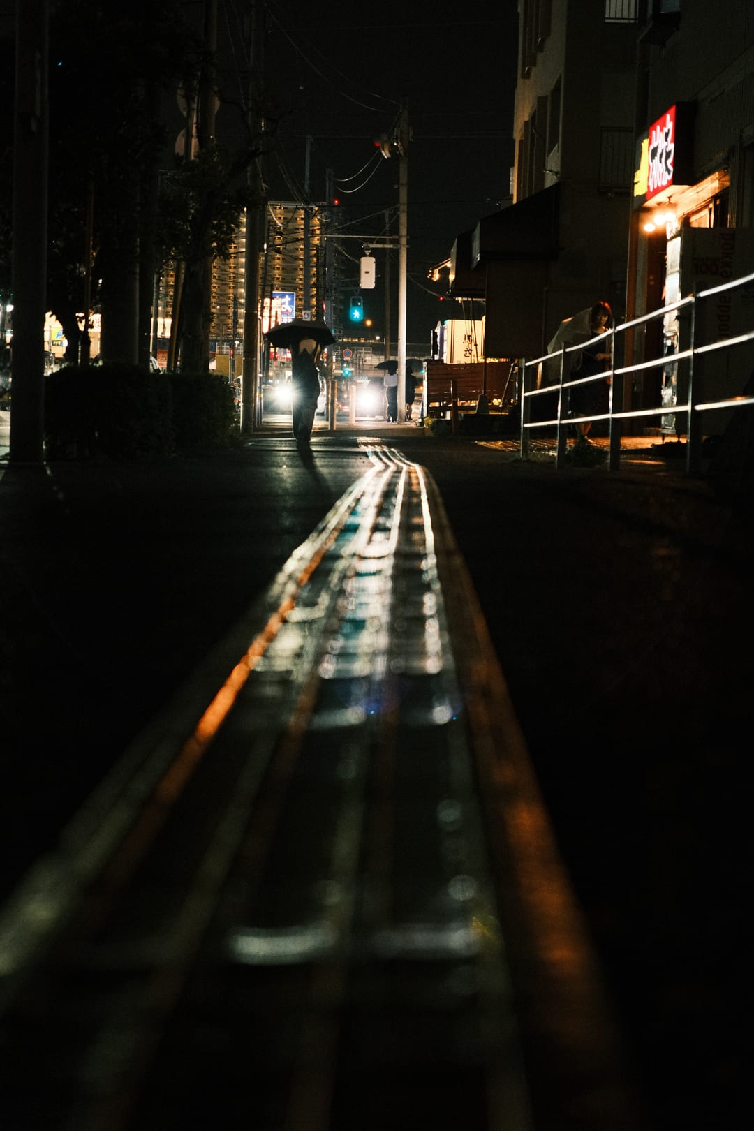 Wet rails and road glinting under streetlights, a figure far ahead