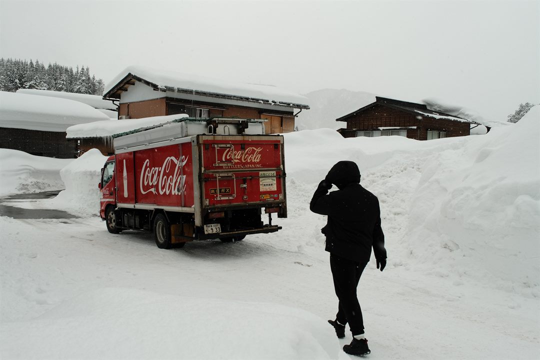 A red delivery truck parked in deep snow as a figure in black walks past