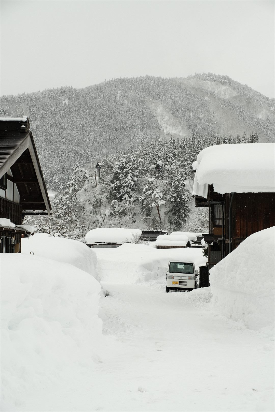 A snowed-in village lane, a small white van buried to its wheels between drifts