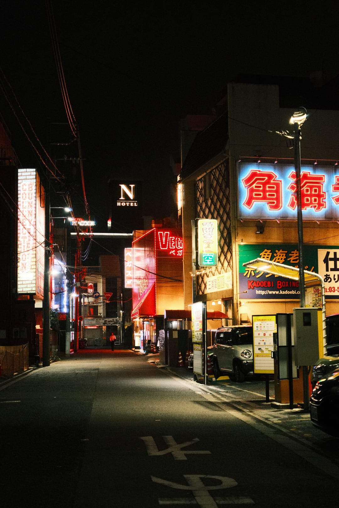 A narrow street of neon signage at night, a car parked in the glow