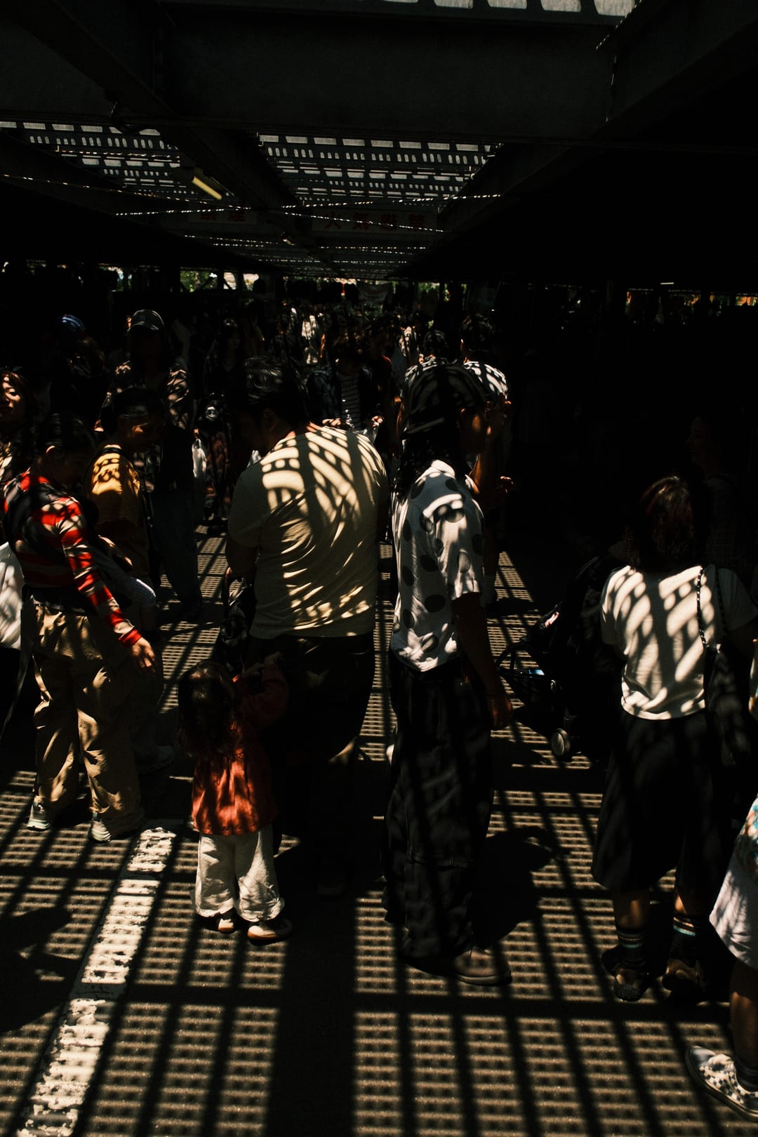 A crowd browsing a market under a grid of light and shadow