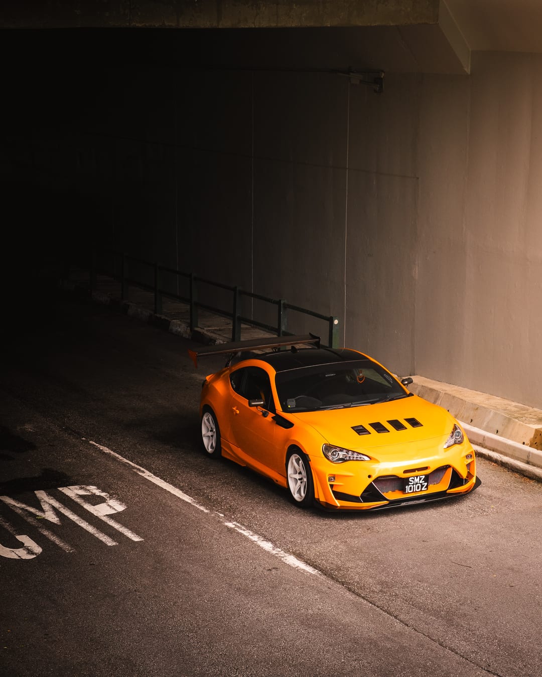 An orange widebody Toyota GT86 on a concrete ramp beneath an overpass