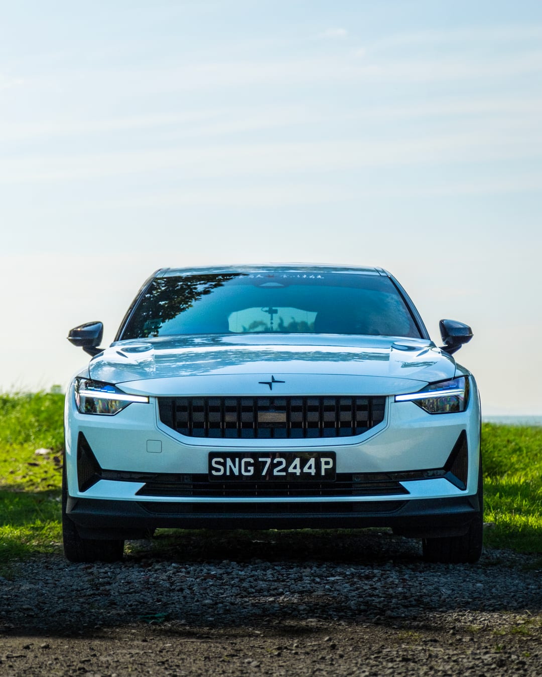 A white Polestar 2 head on beside the water with grass in the foreground
