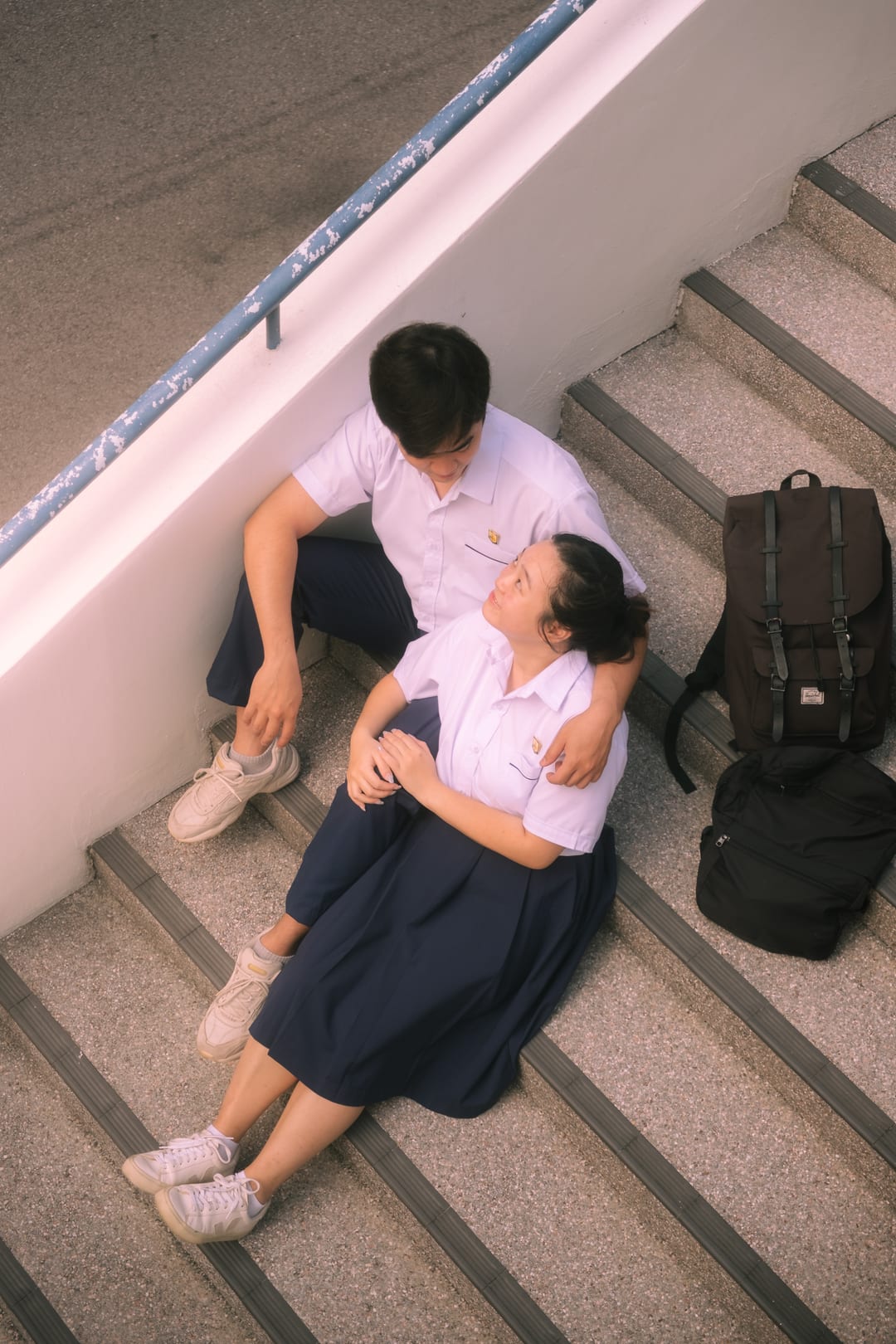 The couple sitting together on a stairwell landing seen from above, their backpacks beside them